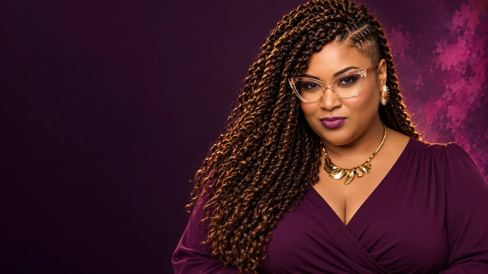 Nina Simmons in a plum wrap dress and cat-eye glasses with gold jewelry and long twists, against a deep plum backdrop